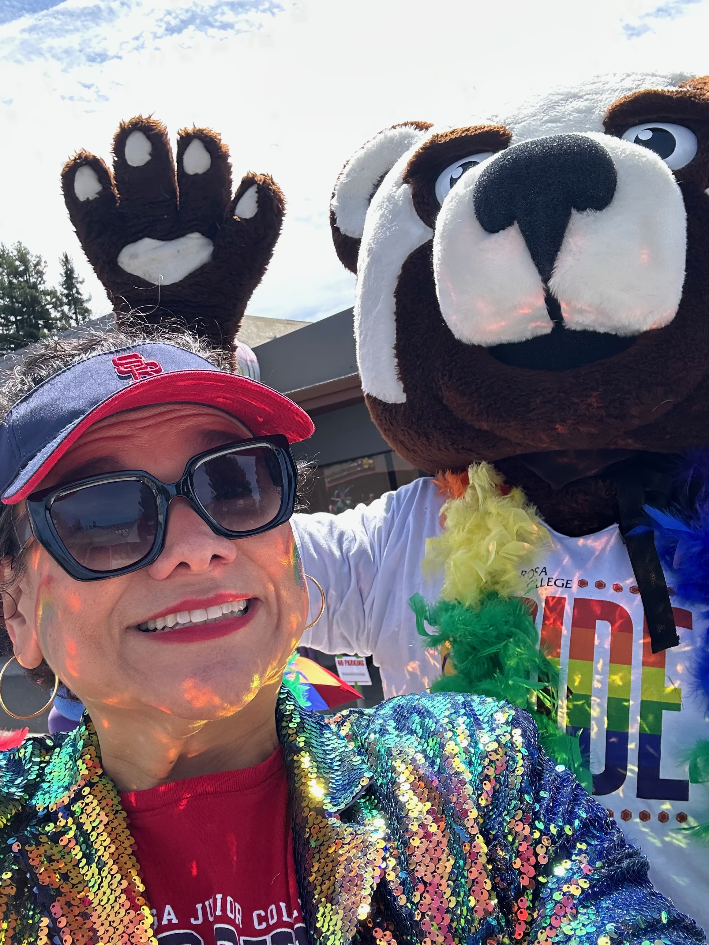 Photo of Dr Angelica Garcia with SRJC's mascot Rosco, dressed in sparkling, colorful Pride clothing